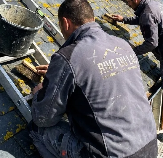Couvreur Rive du Lac brossant à la main les lichens d'une couverture en ardoise à Duingt